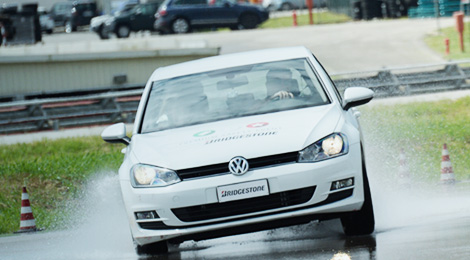 Automóvil Volkswagen blanco con neumáticos Bridgestone en pista mojada Automóvil Volkswagen blanco con neumáticos Bridgestone en pista mojada